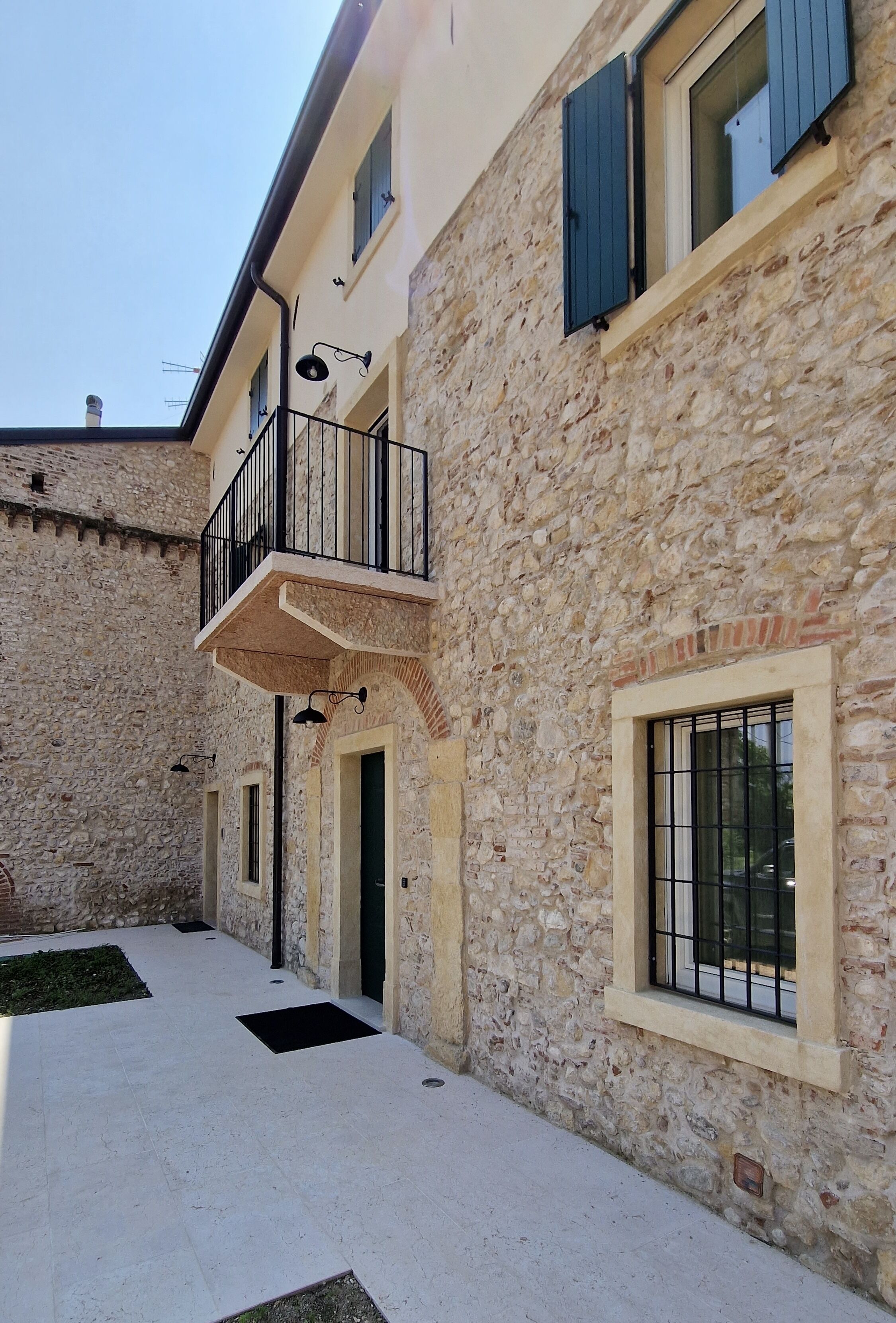 A stone building with a balcony, multiple windows, and a tiled courtyard.