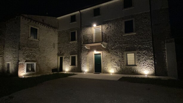 A stone building with a central entrance and multiple windows, illuminated by exterior lighting. - CasaOssan (San Pietro in Cariano)