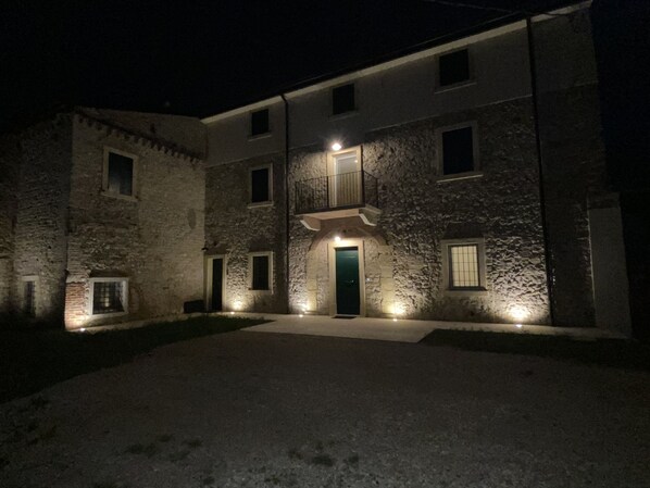 Edifício de pedra com entrada central e várias janelas, iluminado por iluminação externa.