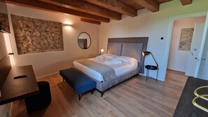 Quarto com cama, mesa de cabeceira, banco, luminária e parede de pedra.