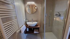 Uma casa de banho moderna com uma bacia branca, um espelho redondo, cabine de duche envidraçada e porta-toalhas.