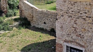 A stone building with a window and a door, surrounded by a vineyard and a stone archway. - CasaOssan (San Pietro in Cariano)