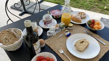 Una mesa servida con alimentos para el desayuno, incluyendo pan, tomates, una botella de aceite de oliva y un vaso de jugo de naranja.
