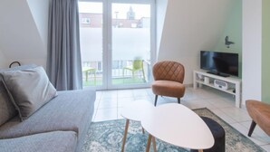 Sala de estar moderna com sofá, uma mesinha, televisão e varanda com vista para edifícios.