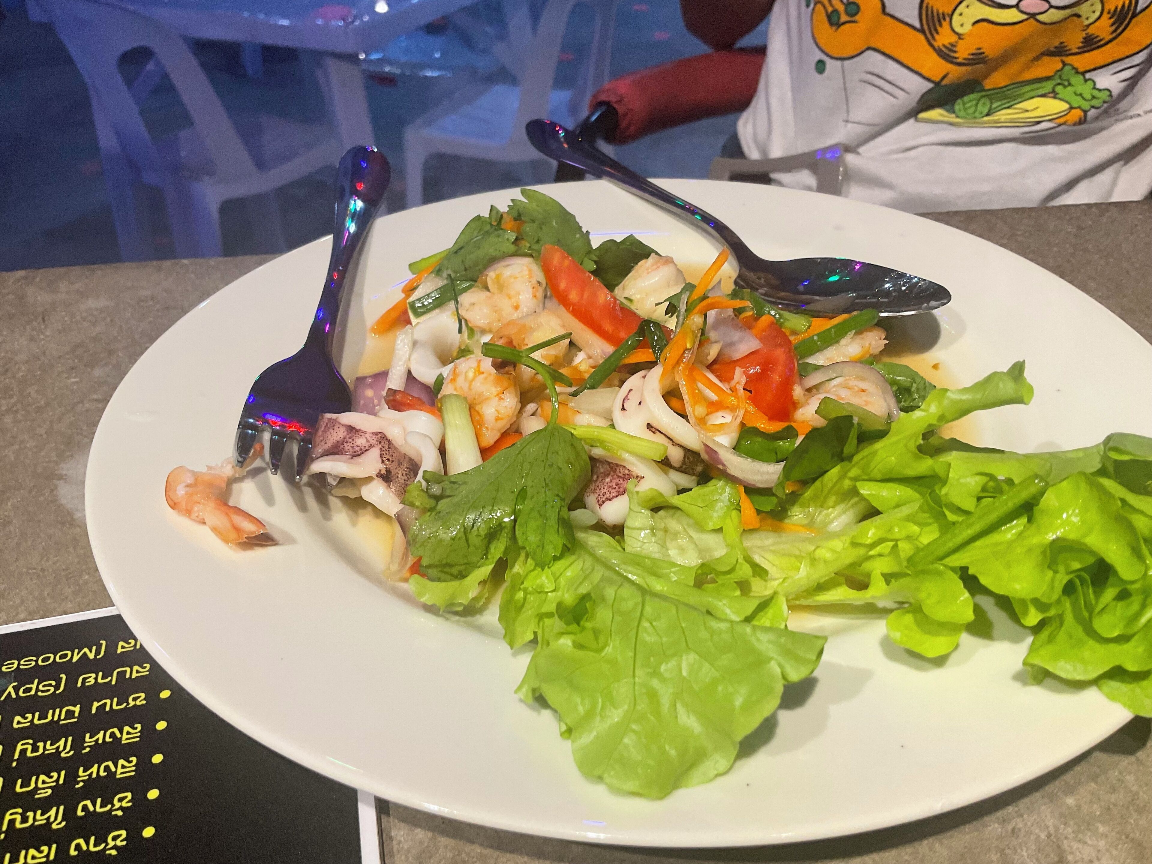 A plate of seafood salad with lettuce and vegetables, accompanied by a fork and spoon.