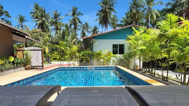 Una piscina con borde de azulejos, rodeada de palmeras y un edificio de fachada blanca.