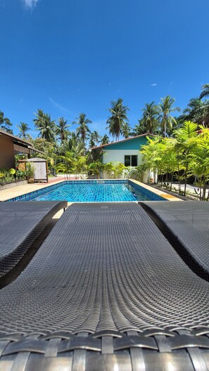 A swimming pool with a tiled edge, surrounded by palm trees and a building with a white facade.