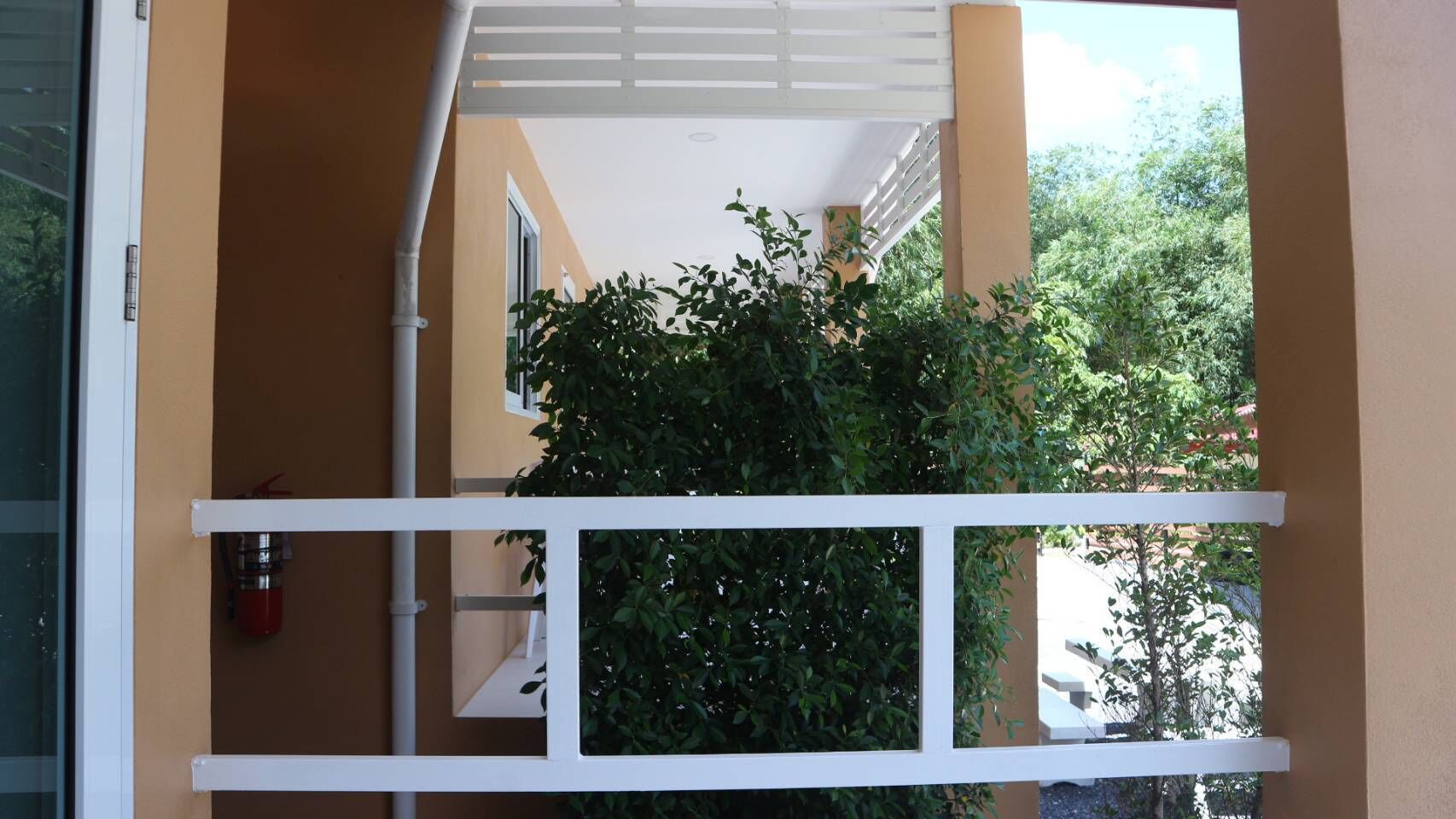 Une balustrade de balcon blanche, avec vue sur un buisson verdoyant et un bâtiment en arrière-plan.