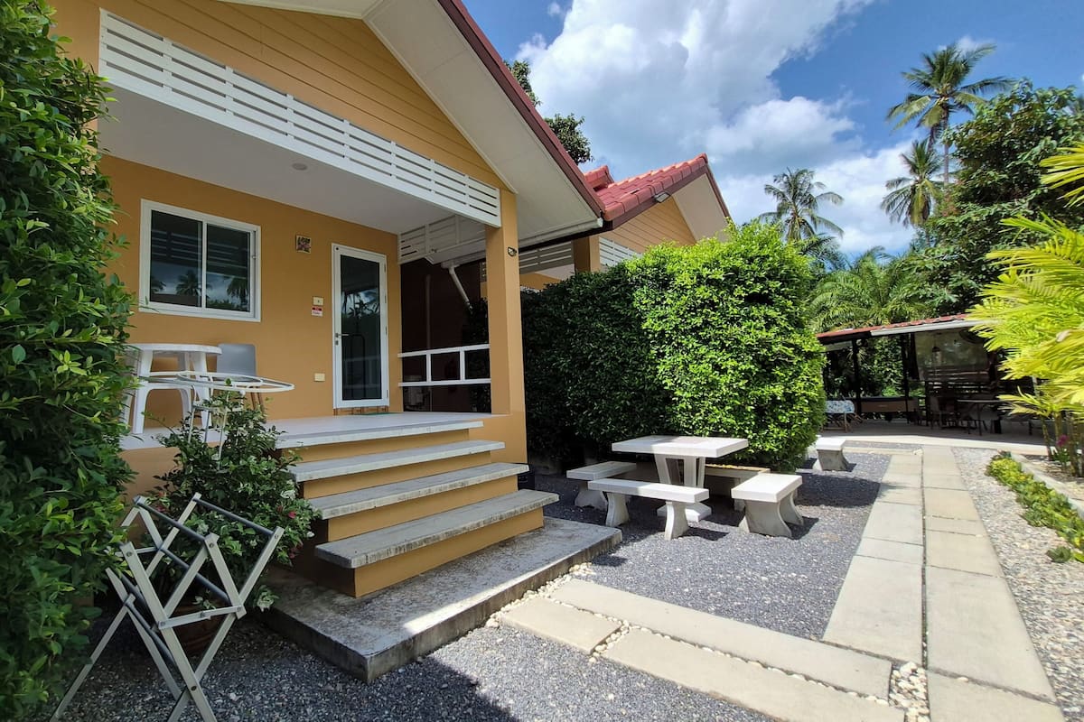 A yellow building with a red roof, a covered outdoor seating area, and a small garden.