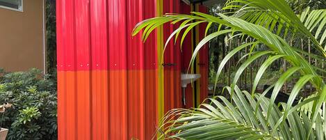 A cylindrical structure with a red and orange color scheme, a sink, and is surrounded by greenery.