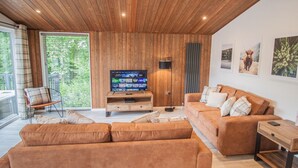 Una sala de estar moderna con techo de madera, un televisor de pantalla plana grande, un juego de sofá y una lámpara de pie.