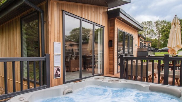 Una cabaña de madera con jacuzzi, puertas corredizas de vidrio y mobiliario exterior.