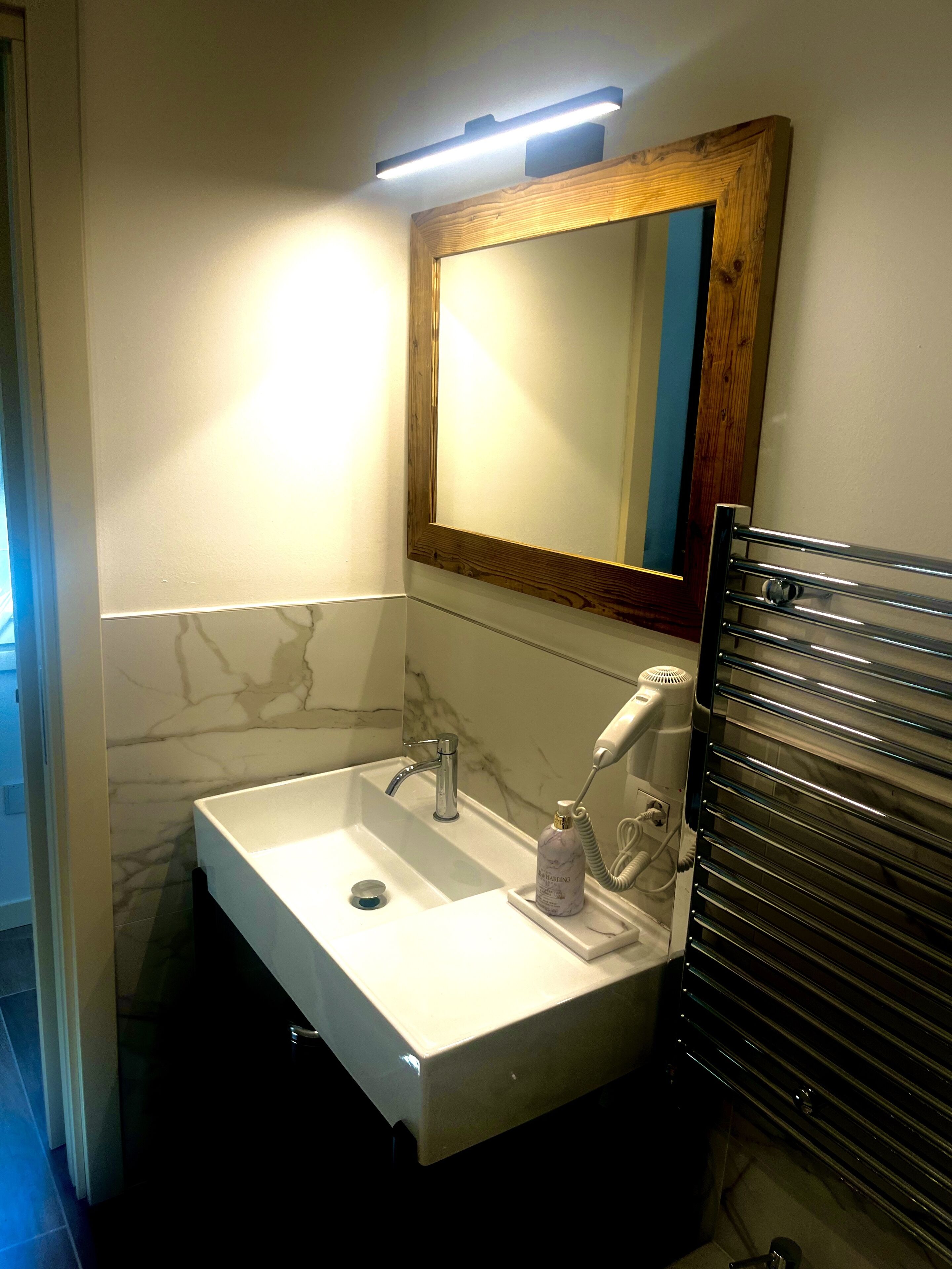 A bathroom with a white sink, a mirror with a wooden frame, a towel rack, and a hairdryer.