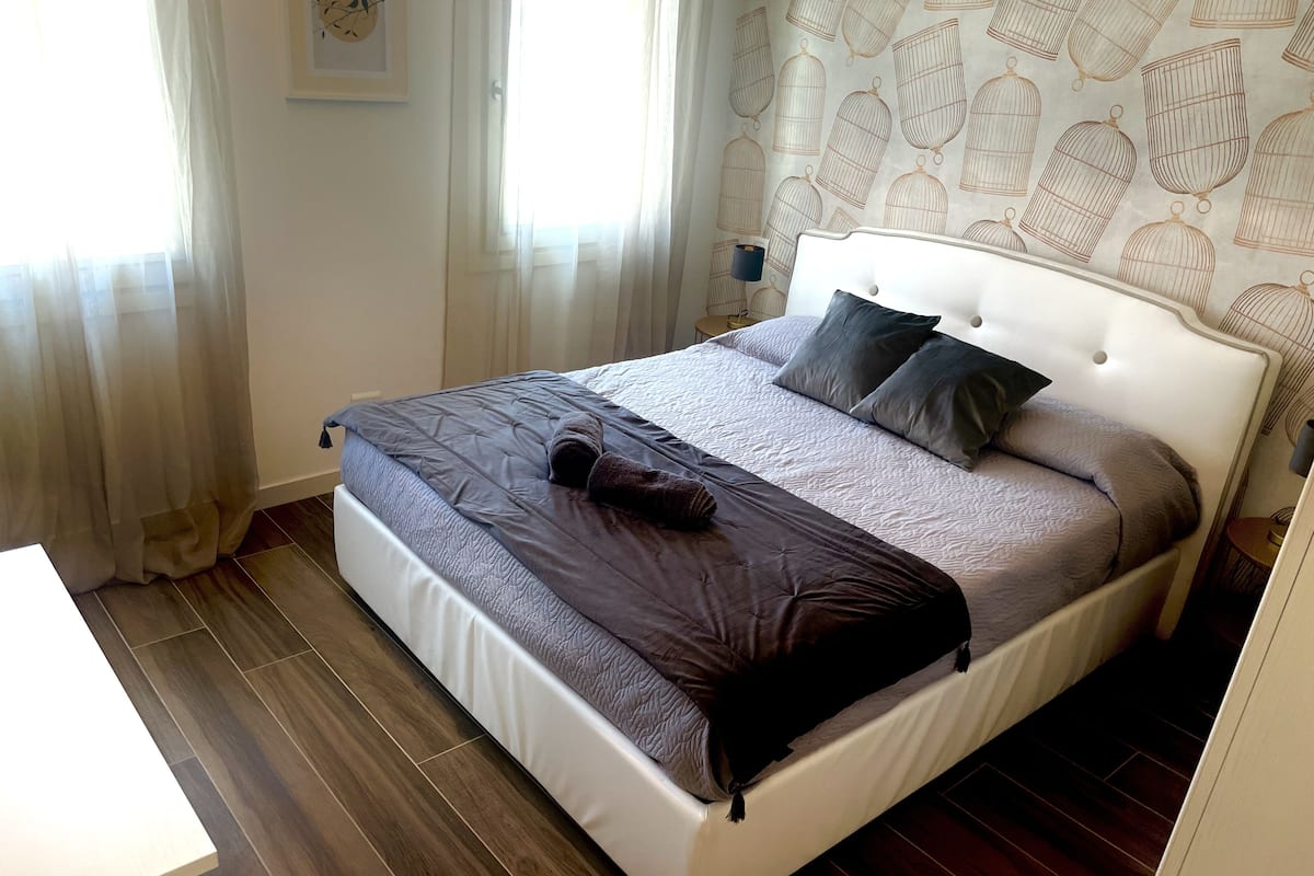 A neatly made bed with a white headboard, a grey and brown blanket, and two pillows.