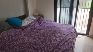 Une chambre à coucher avec un lit, des oreillers, une table de chevet et une fenêtre donnant sur un paysage verdoyant.