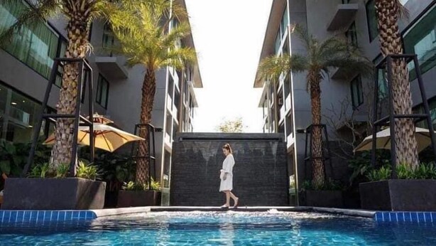 A pool area with a person walking, surrounded by palm trees and modern buildings. - Vacation Home Rental The Starhill Condo Chiang Mai (Muang Chiangmai)