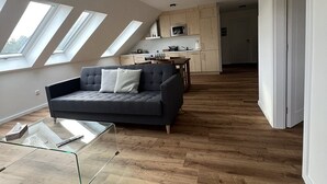 A modern loft apartment with a dark grey sofa, a glass coffee table, wooden flooring, and skylights.