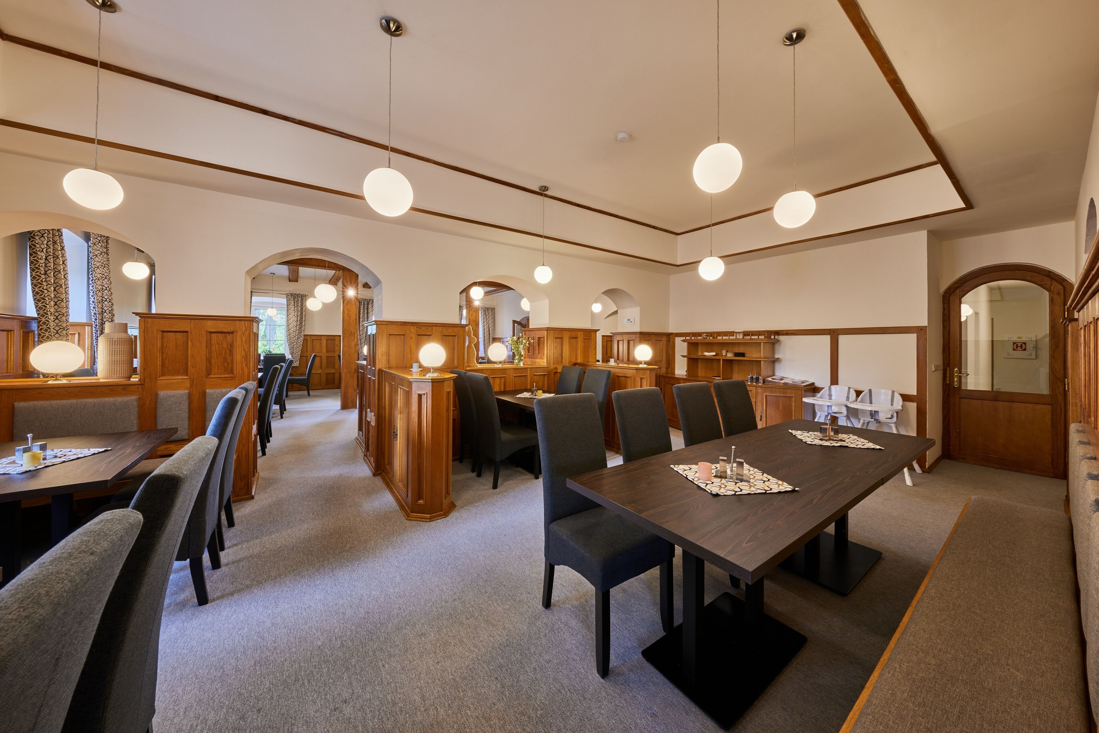 Un comedor amplio con mesas y sillas altas, armarios de madera e iluminación colgante.