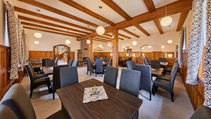 A spacious dining area with wooden beams, round pendant lights, and a central table with a placemat.
