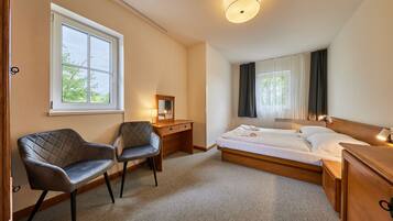 A hotel room with a bed, a desk, two chairs, a mirror, and a window with curtains.