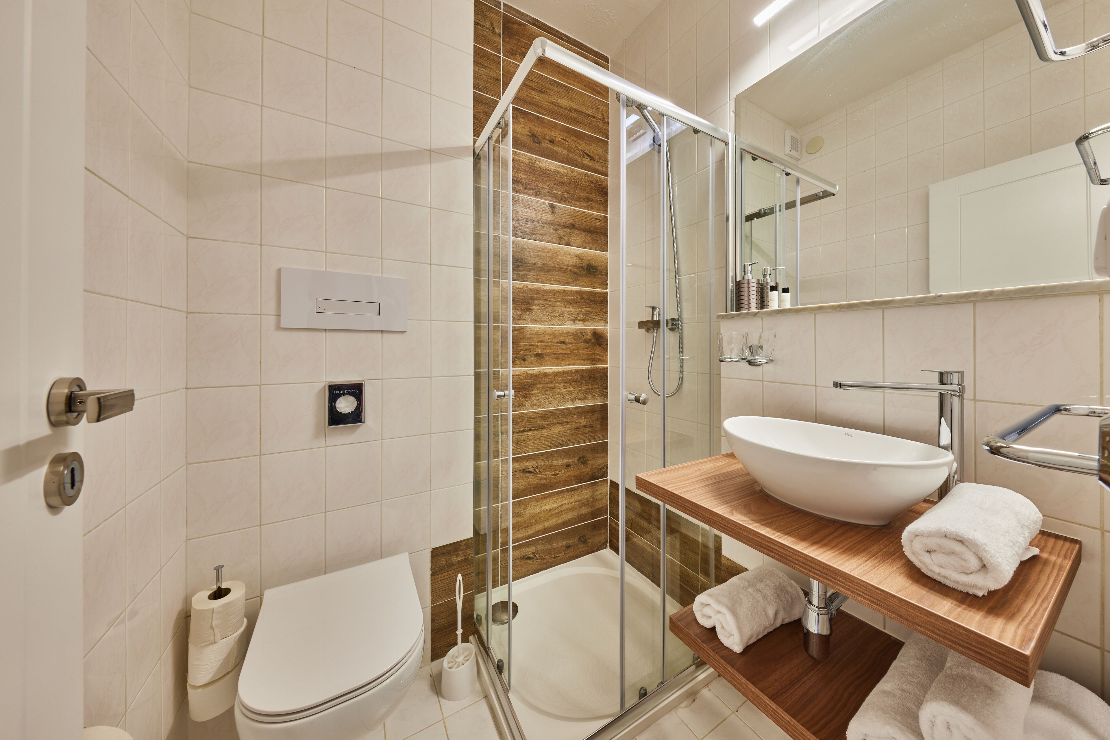 Een moderne badkamer met een glazen douchecabine, een houten wastafelmeubel met een wastafel en een toilet.