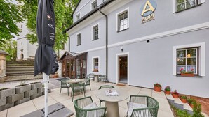A courtyard with outdoor seating, a flag, and a building with a sign.