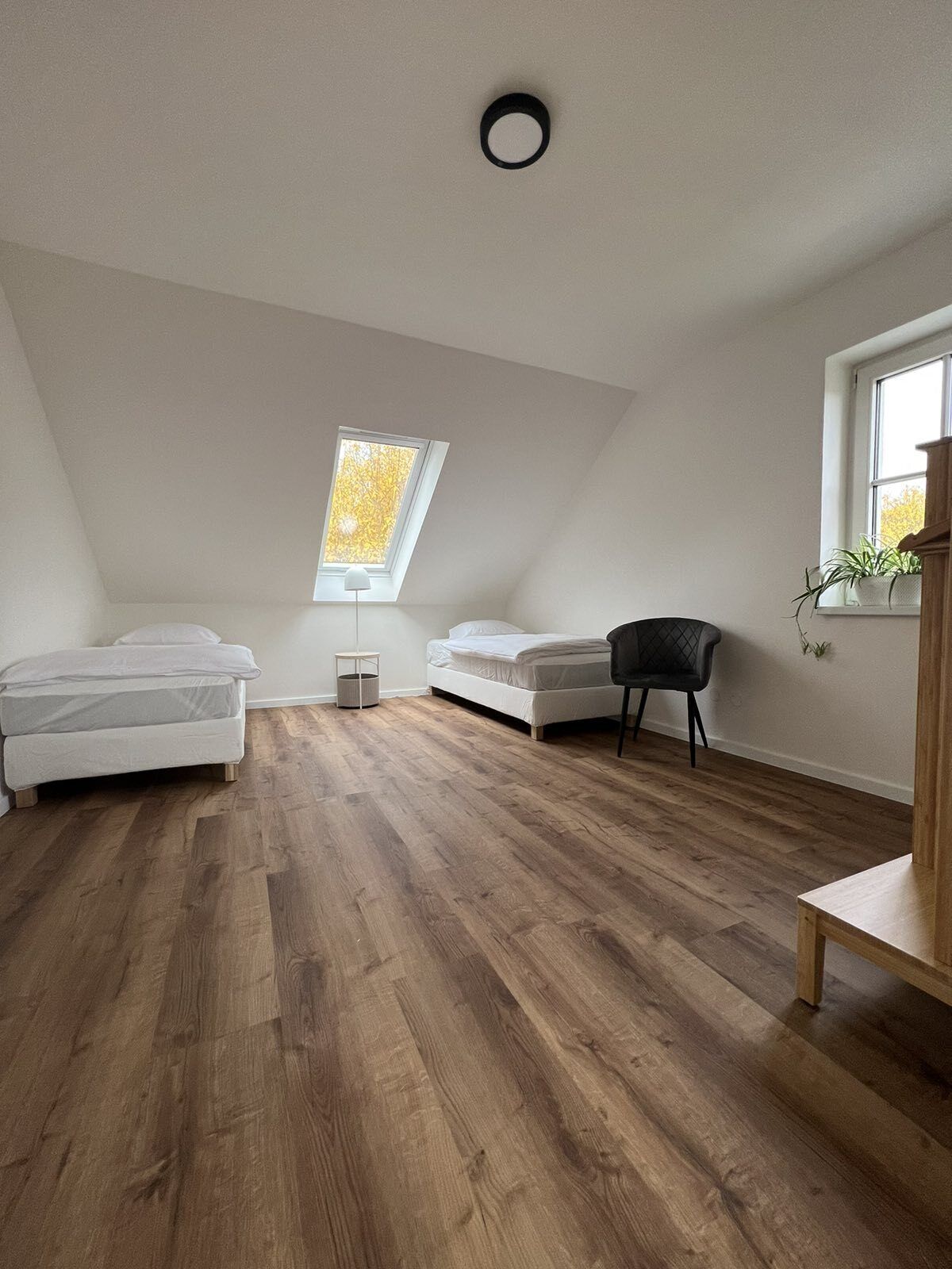 A room with a sloped ceiling, a skylight, a bed, a chair, and a small table.