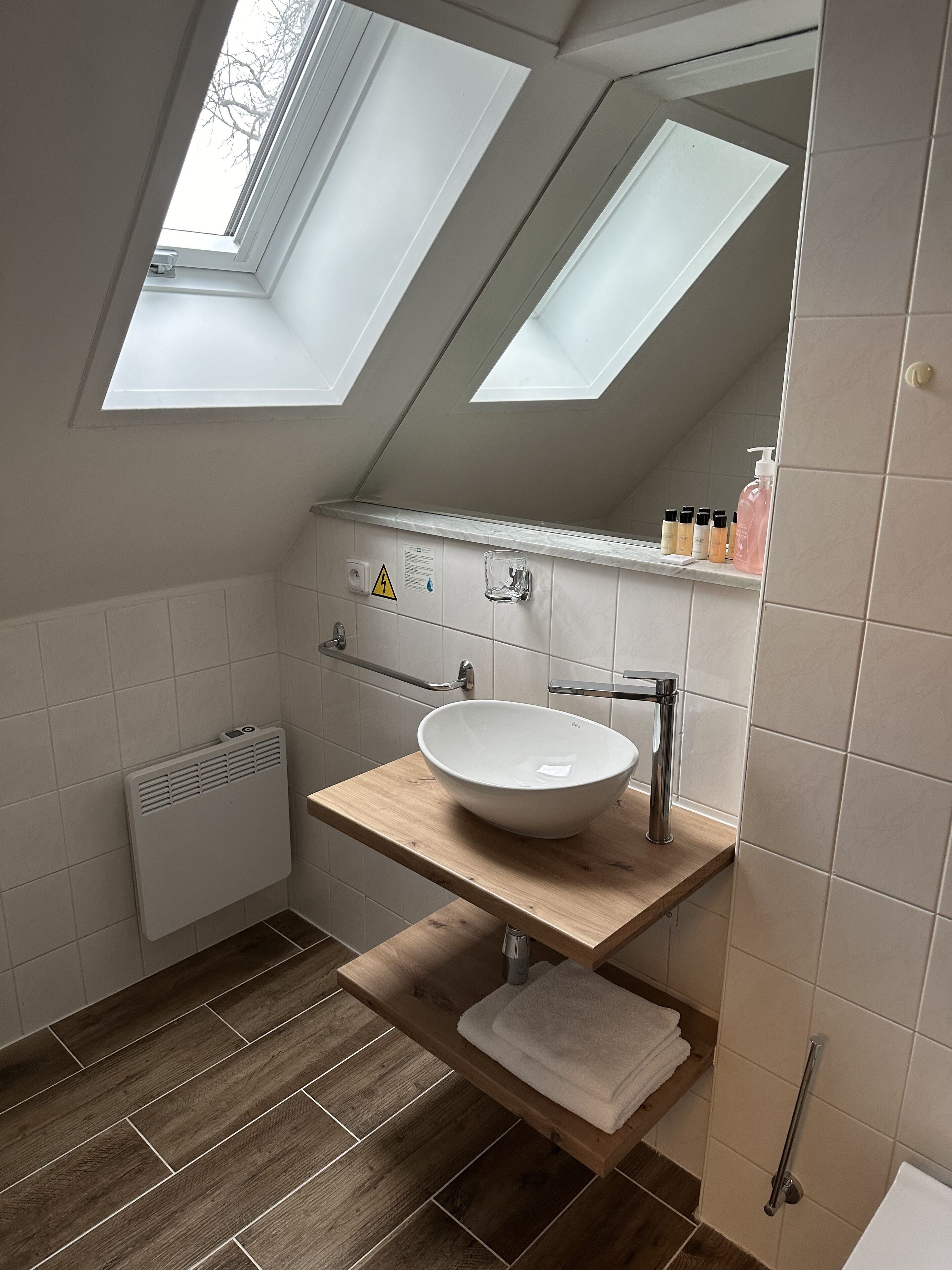 A modern bathroom with a skylight, a white sink, and a wooden vanity.