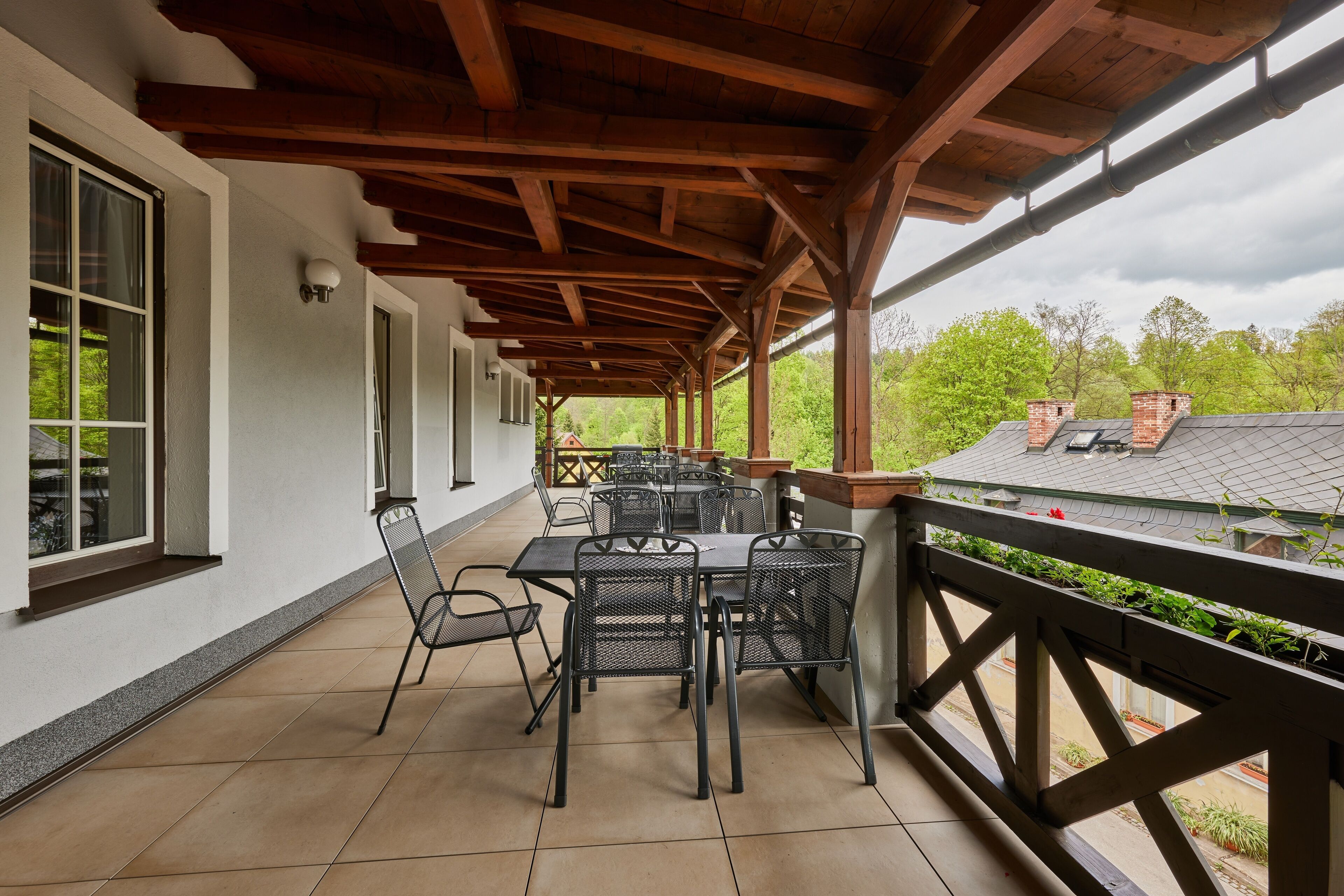 Patio esterno con pergola in legno, pavimento piastrellato e tavoli e sedie in metallo.