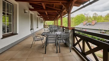 Patio esterno con pergola in legno, pavimento piastrellato e tavoli e sedie in metallo.