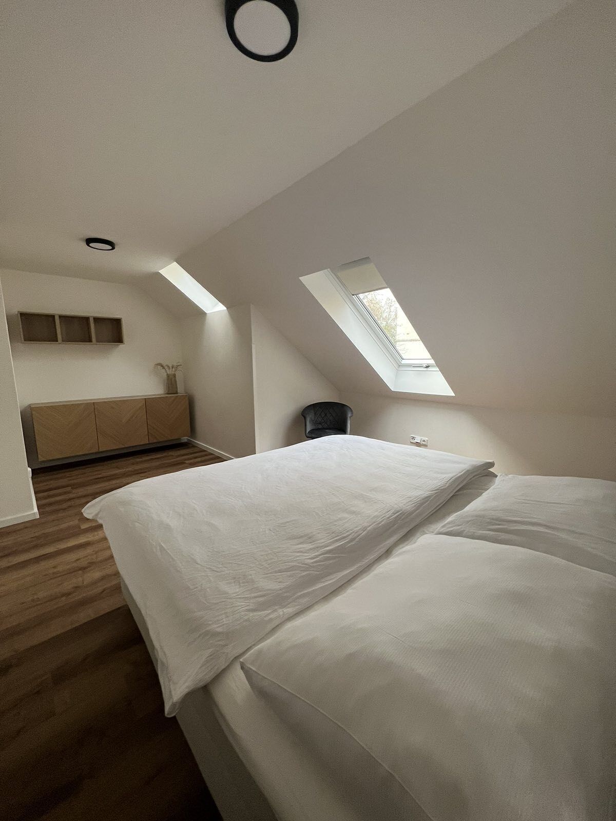 Quarto com claraboia, cama, guarda-roupa e mesa de cabeceira.