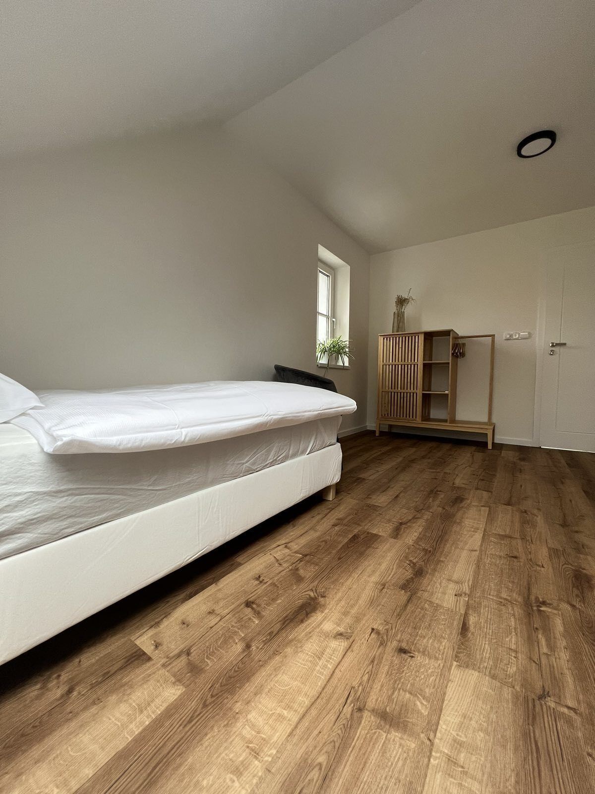 A bedroom with a bed, wooden flooring, a window, and a wardrobe.