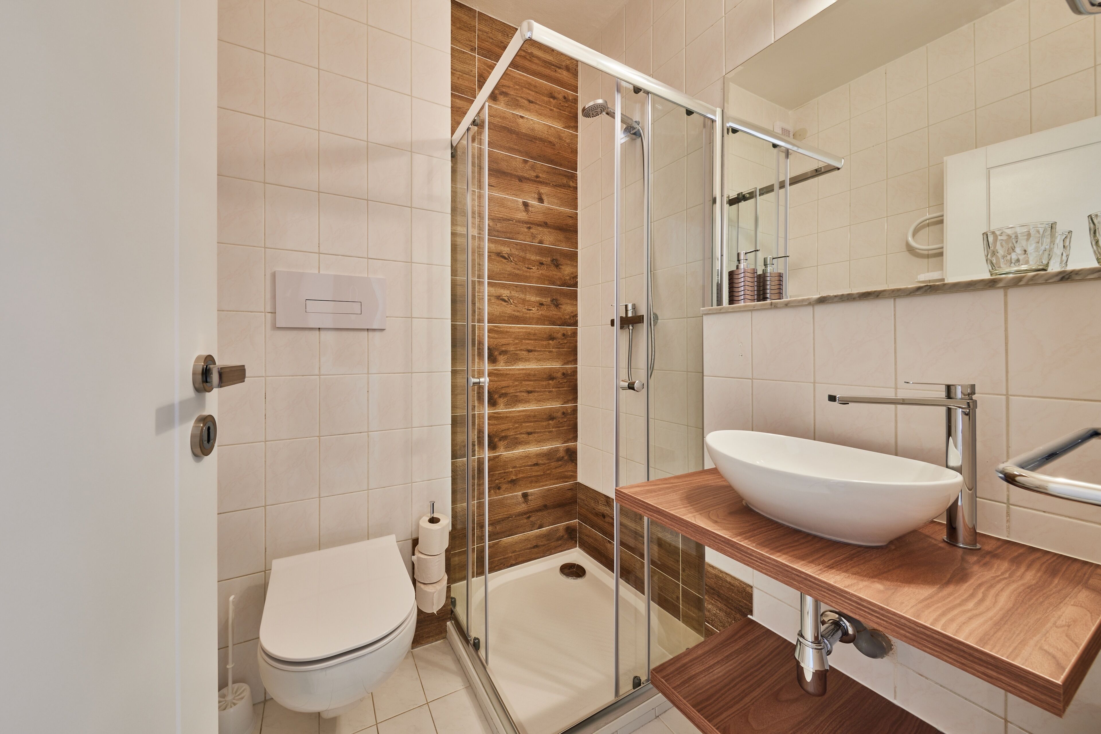 A modern bathroom with a glass-enclosed shower, a wooden vanity, and a white sink.