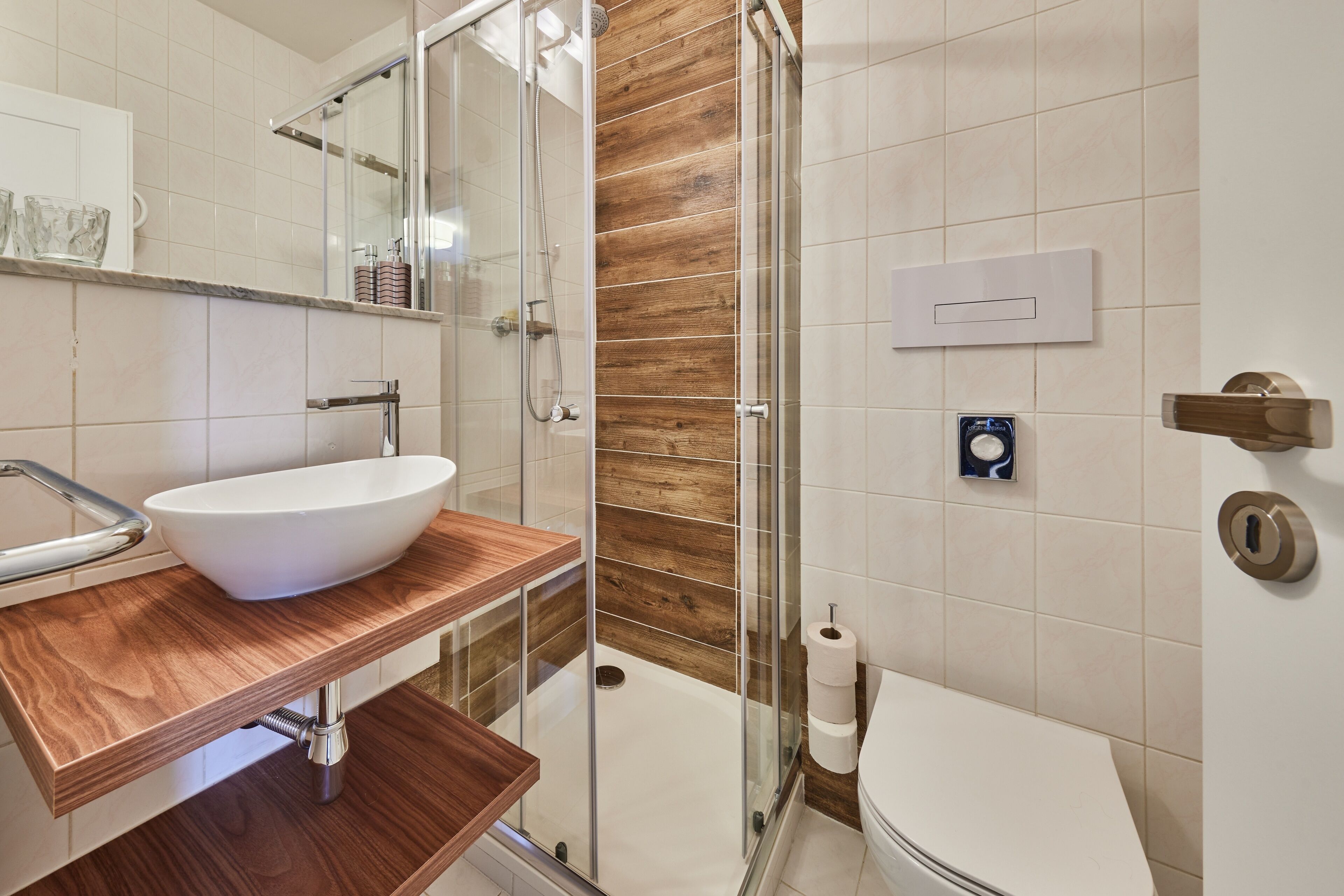 A modern bathroom with a glass shower enclosure, a wooden vanity, a white sink, and a toilet.