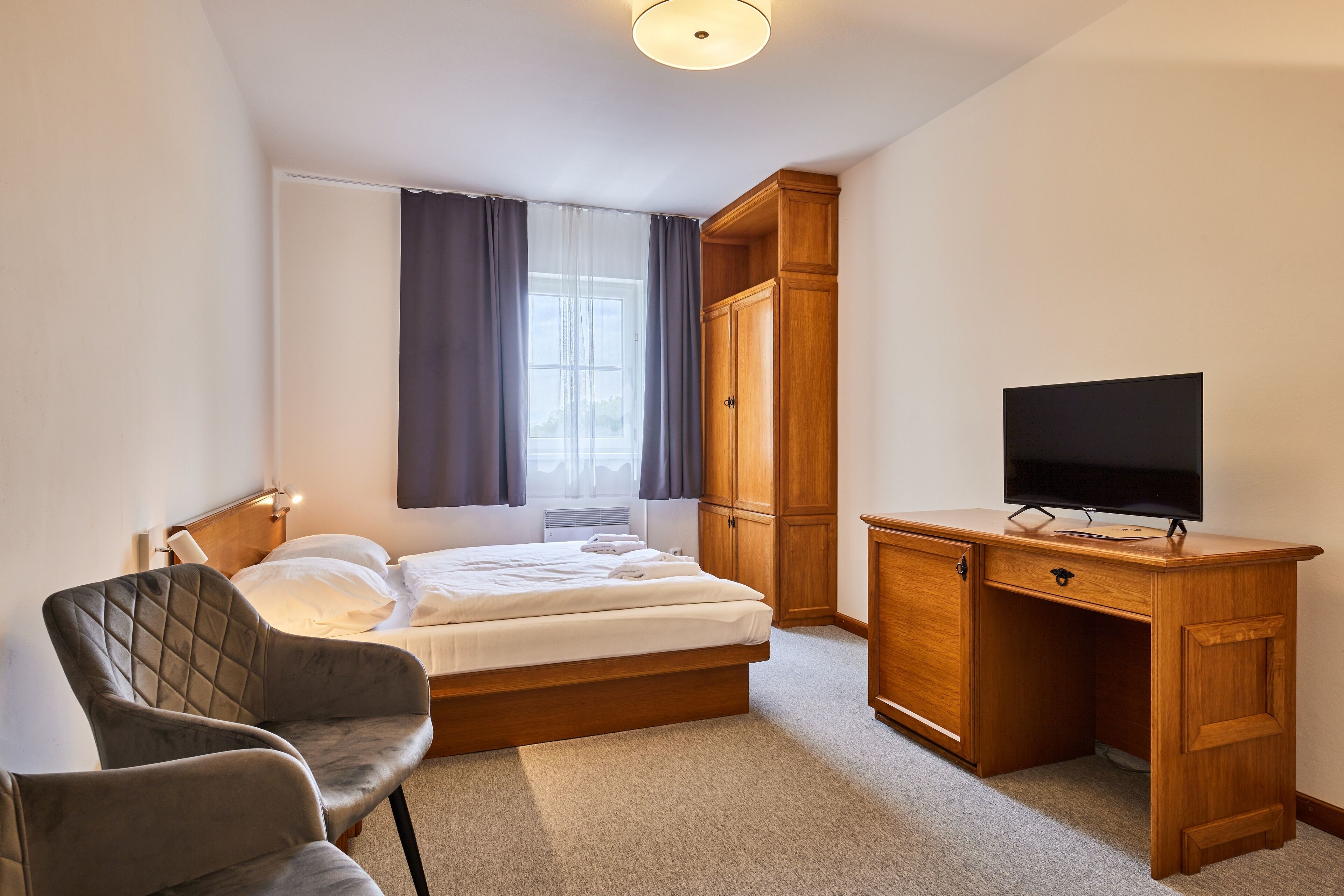 A bedroom with a bed, a desk with a television, a chair, and a wardrobe.