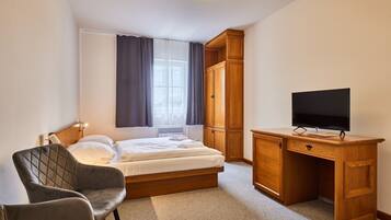 A bedroom with a bed, a desk with a television, a chair, and a wardrobe.