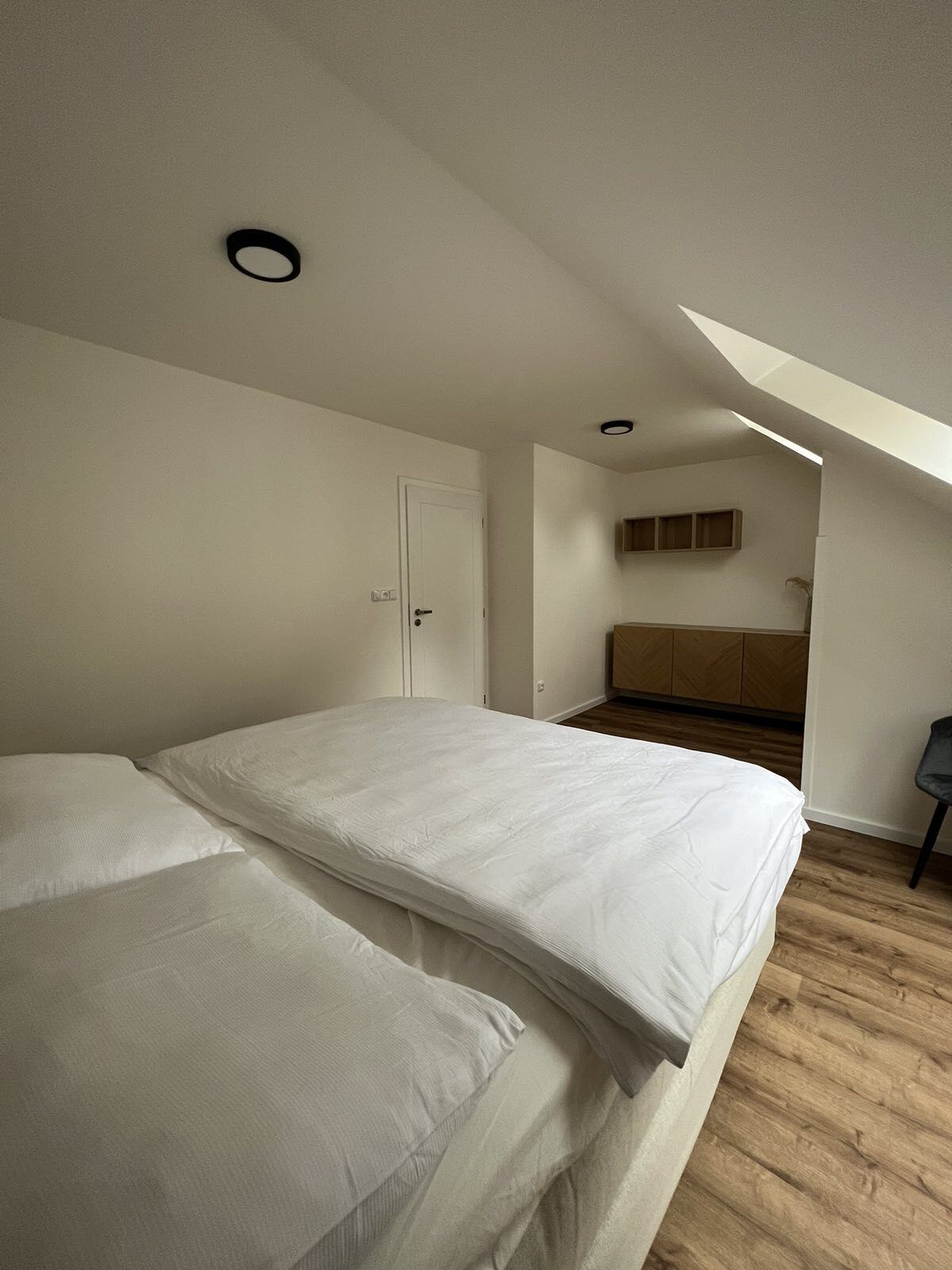 A bedroom with a large bed, a door, a wooden cabinet, and a skylight.