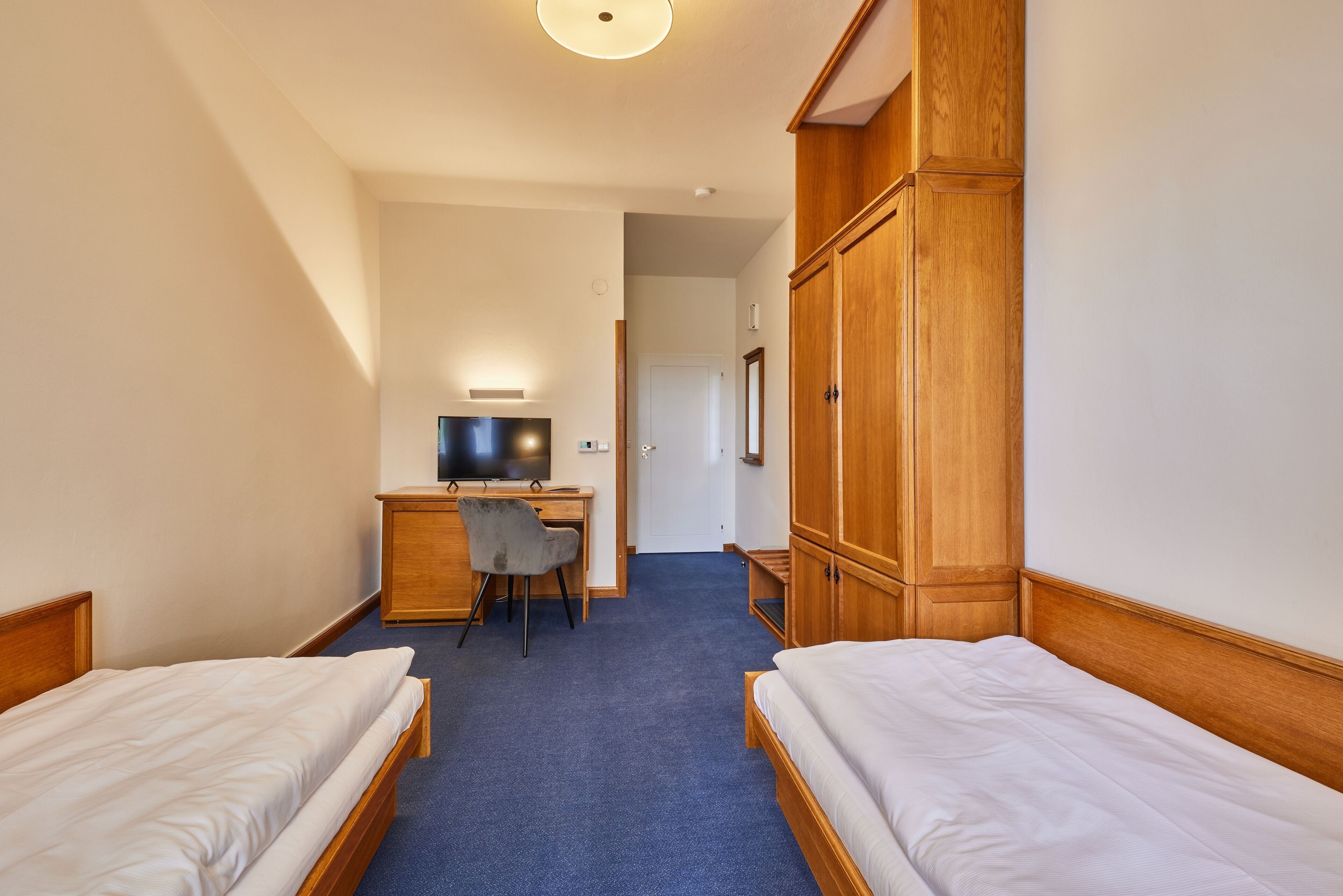 A hotel room with two single beds, a desk with a chair, a television, and a wardrobe.