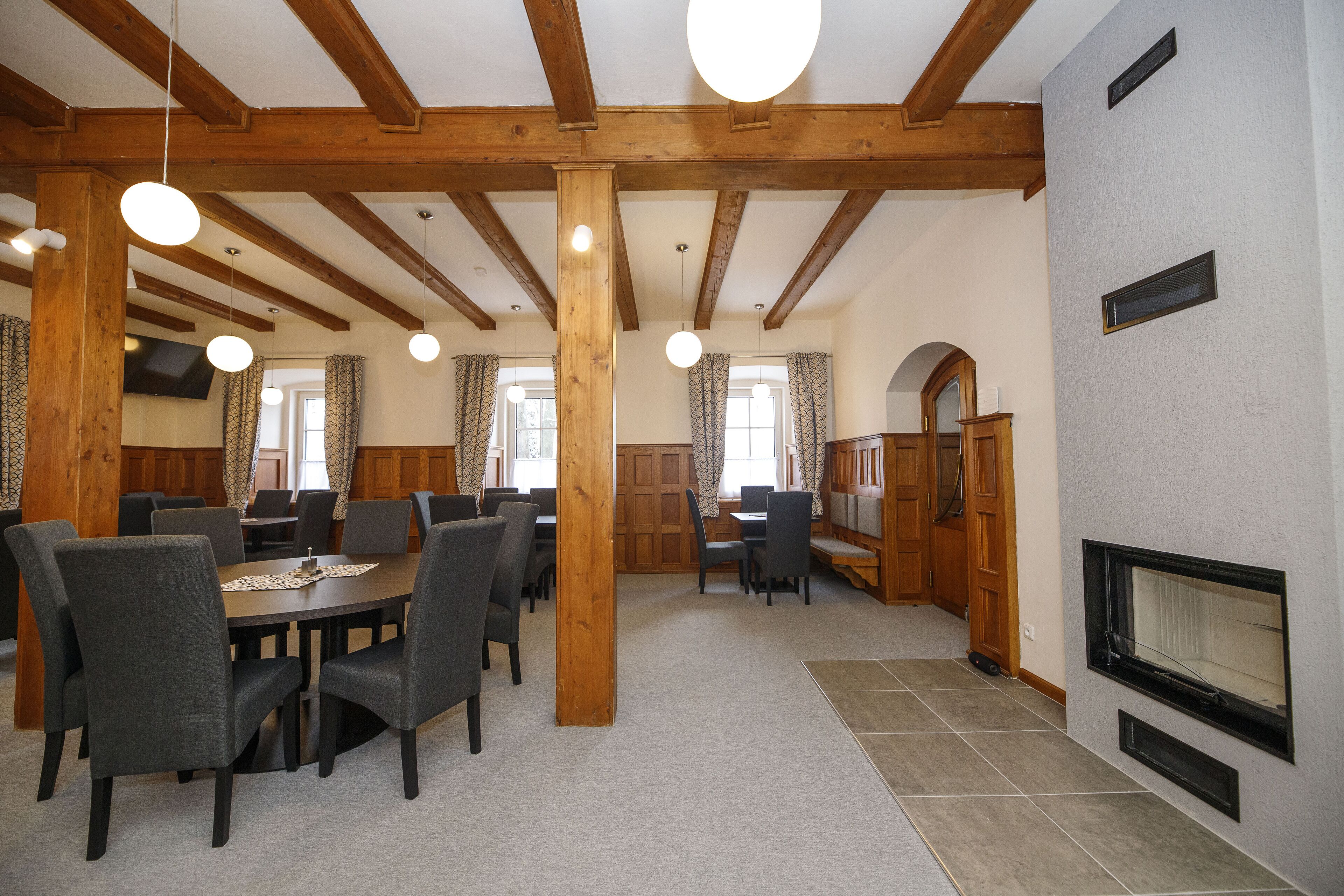 A spacious dining area with wooden beams, round ceiling lights, and a fireplace.