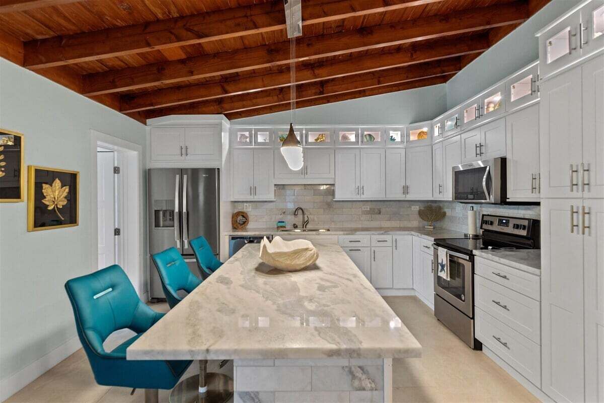 Een moderne keuken met witte kasten, een marmeren eiland en een houten plafond.