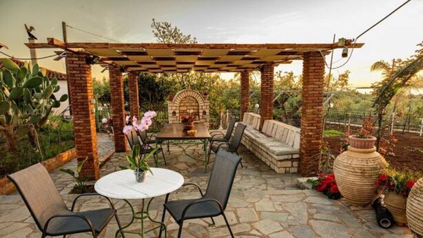 An outdoor patio with a brick pergola, stone flooring, a round table with chairs, and potted plants. - Χαλαρώστε σε ένα ιδιωτικό μέρος 1χλμ απ'τη θάλασσα (Gargalianoi)