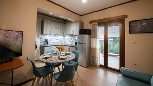 A modern kitchen with white cabinets, a black microwave, and a dining area with a round table and blue chairs. - Χαλαρώστε σε ένα ιδιωτικό μέρος 1χλμ απ'τη θάλασσα (Gargalianoi)