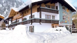 A two-story chalet with a snow-covered roof and wooden balconies, set against a mountainous backdrop. - Ferienwohnung Kaiserin (Reit im Winkl)