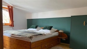 A bedroom with a wooden bed, a green headboard, a nightstand, and a wardrobe. - Ferienwohnung Kaiserin (Reit im Winkl)