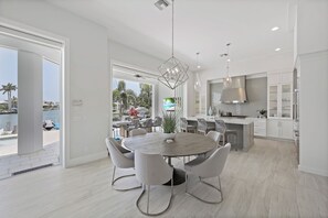 Een moderne keuken met witte kastjes, een centraal eiland en een eetgedeelte met een ronde tafel en stoelen.