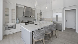 Una cocina moderna con armarios blancos, una isla grande, electrodomésticos de acero inoxidable y taburetes de mimbre.