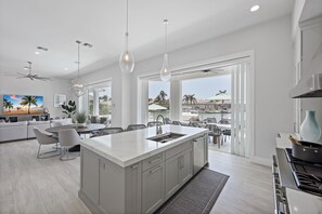 Een moderne keuken met een groot eiland, een eetgedeelte met stoelen en uitzicht op de omgeving.