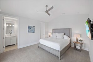 A bedroom with a bed, a ceiling fan, a bedside table with a lamp, and a large mirror.