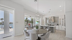 Una cocina moderna con armarios blancos, una isla central y un comedor con una mesa redonda y sillas.