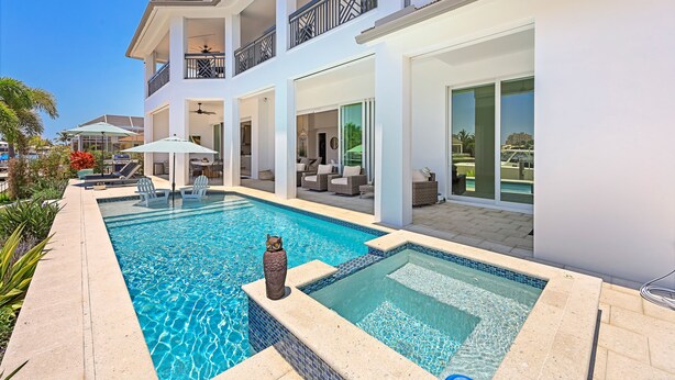 Una casa moderna de dos pisos con piscina, mobiliario exterior y un balcón.